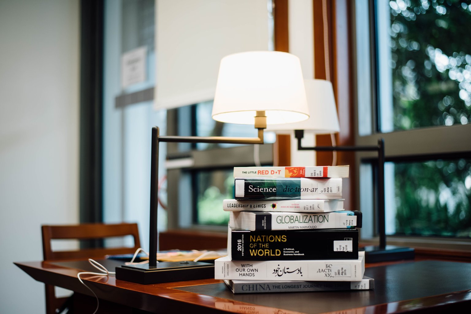 A stack of closed hardback books resting on a table in soft daylight.